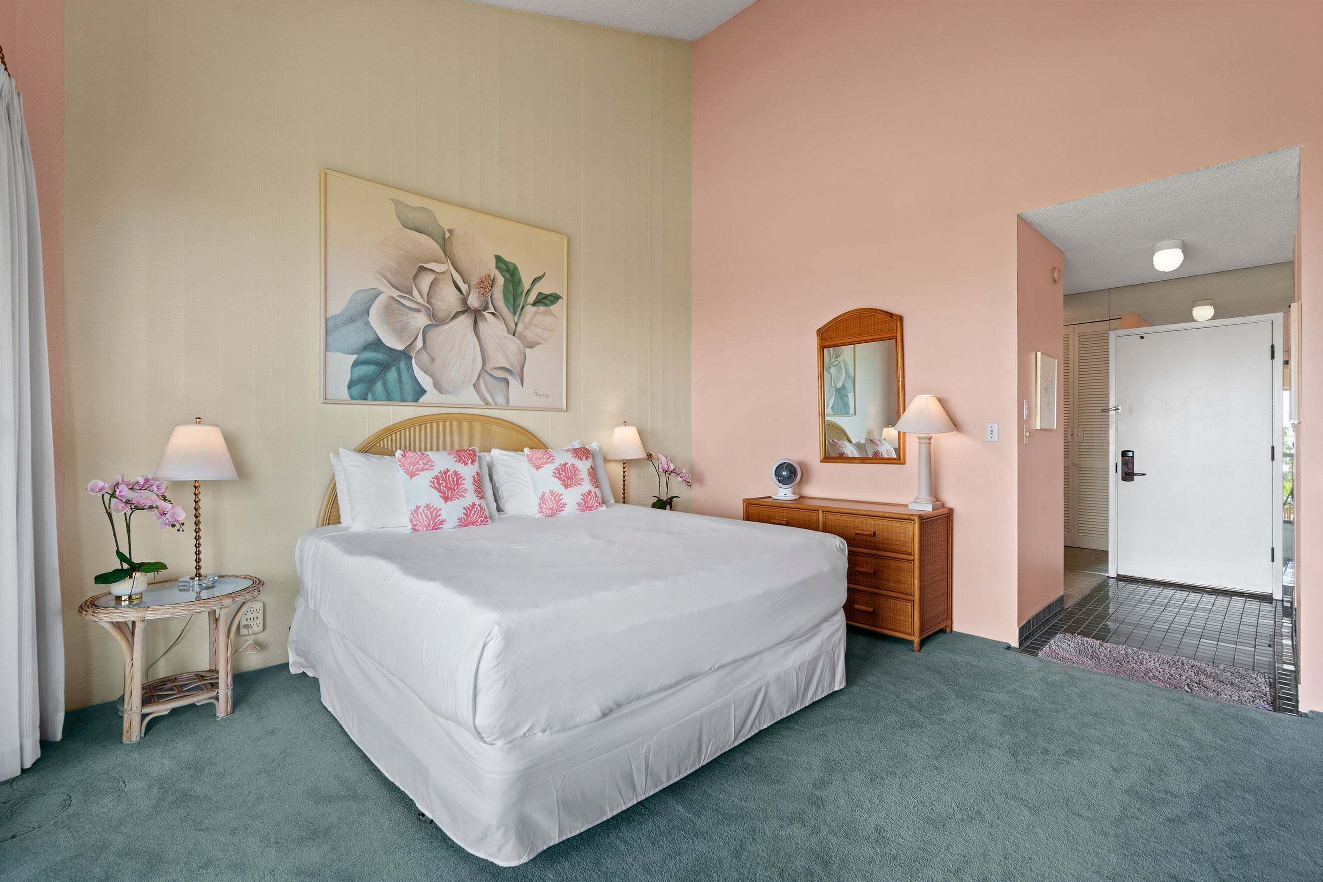 A neatly arranged bedroom with a bed, bedside tables, a dresser, a mirror, and a door leading to another room.