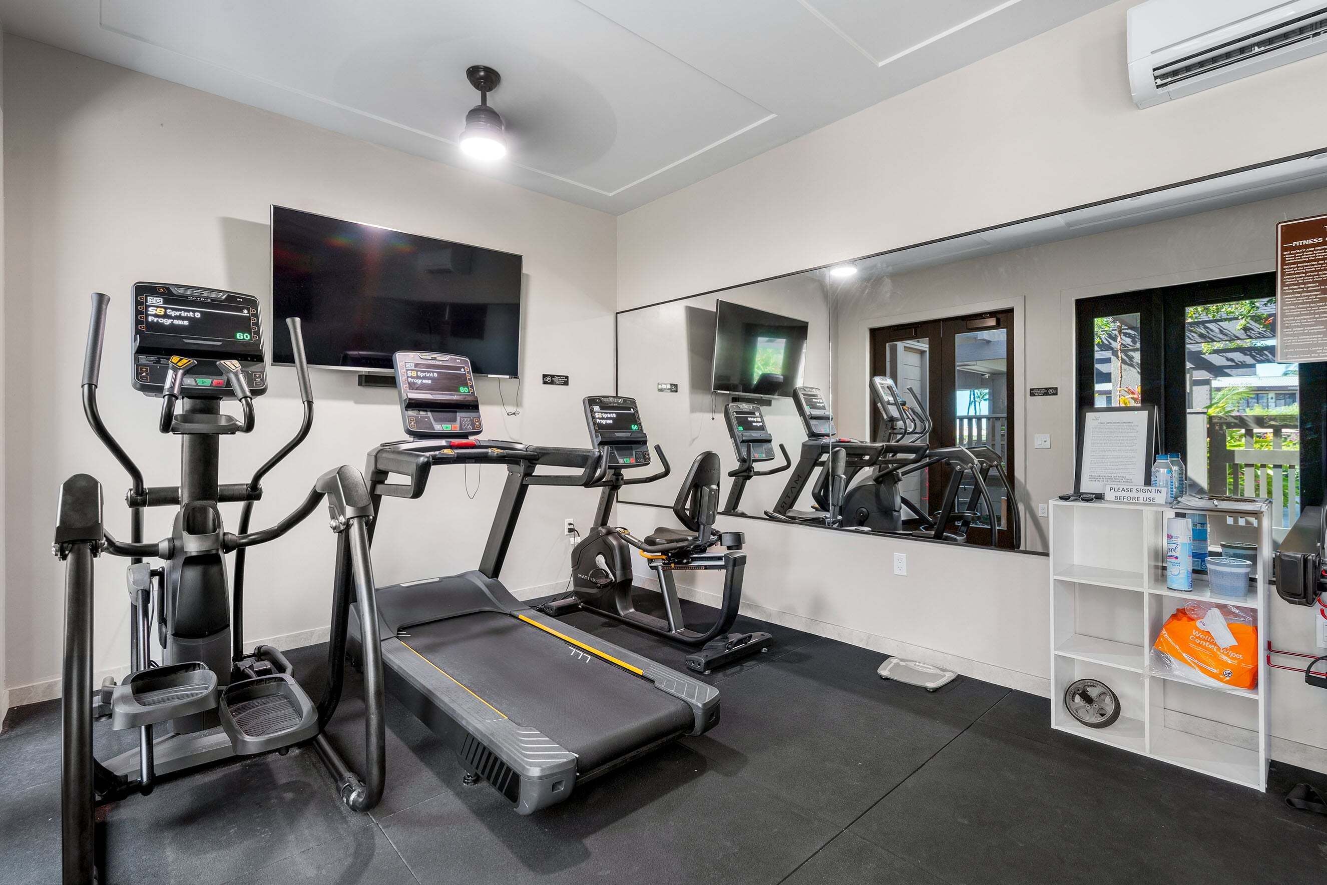 Een fitnessruimte met loopbanden, elliptische trainers en een spiegelwand.
