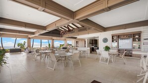 A spacious indoor area with multiple dining tables and chairs, a kitchen area, and a view of the ocean. - Wailea Ekahi 12D - Budget Friendly Ocean View Studio w/ Lanai, Kitchen, WD, & AC (Kihei)