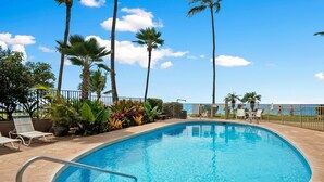 A swimming pool with a curved edge, surrounded by palm trees and lounge chairs. - Kamaole Nalu 301 - Stunning Ocean Views, Renovated, Ocean Front, New Listing! (Kihei)