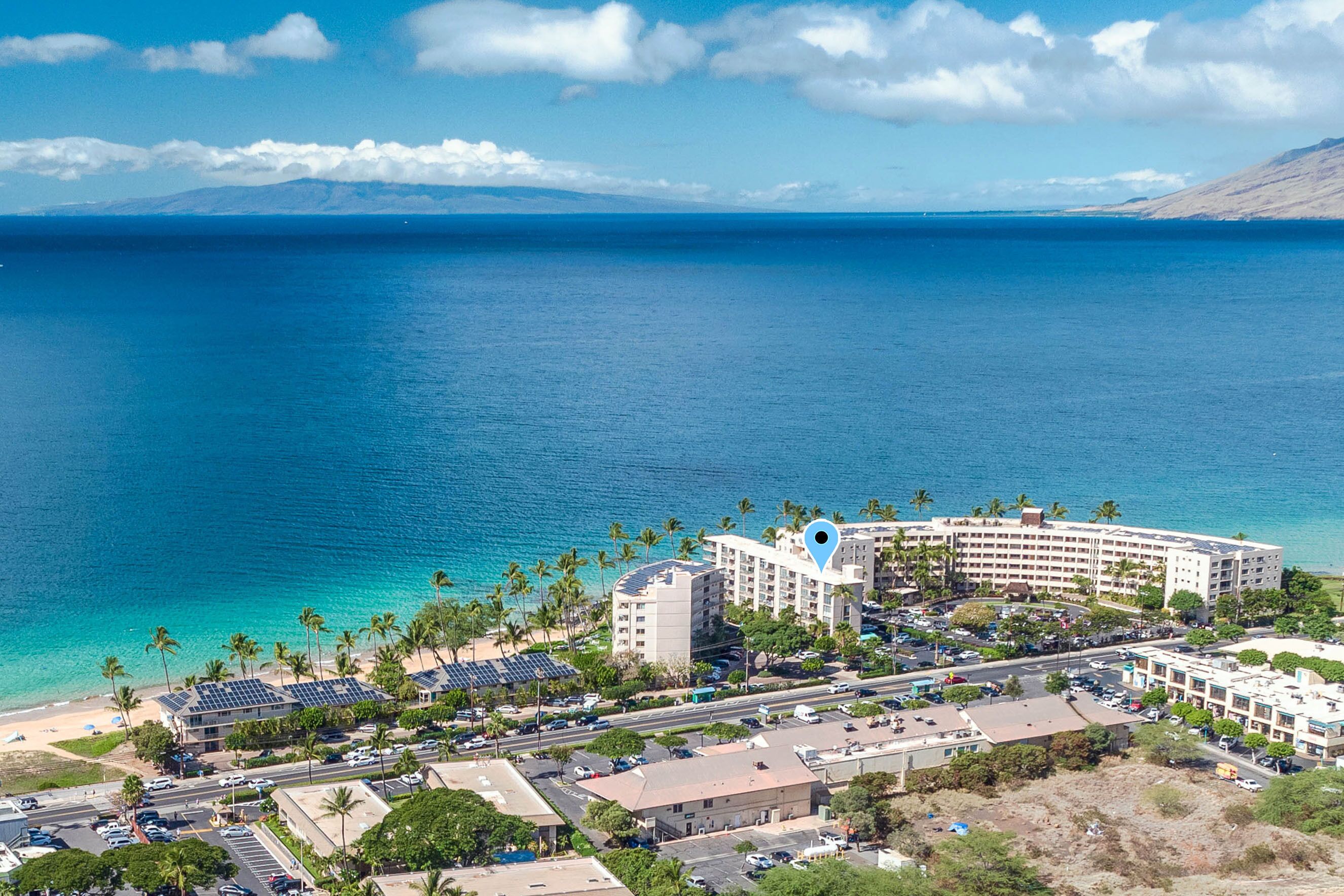 A coastal hotel with a central building, a parking lot, and a beach area.