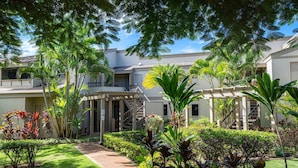 A multi-story hotel with a covered walkway, lush greenery, and a clear sky. - Dramatic Ocean Views, Wailea Ekolu 407, Perfect for Couples, Renovated, Split AC (Kihei)