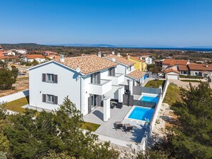 Ein modernes, zweistöckiges Haus mit Swimmingpool, umgeben von Grünflächen und freiem Blick auf die Landschaft.