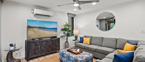 Un salon moderne doté d’un téléviseur à écran plat, d’un ventilateur de plafond et d’une grande fenêtre.