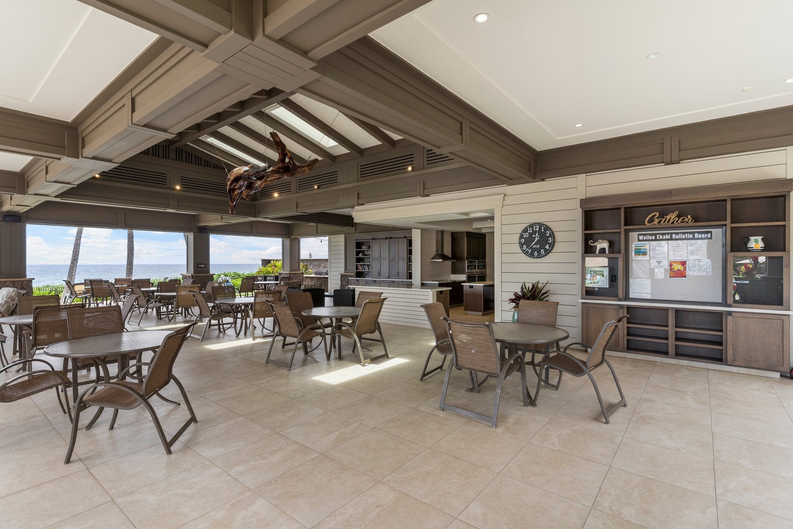 A spacious indoor dining area with multiple tables and chairs, a kitchen area, and a bulletin board with various notices.