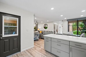 A modern kitchen with grey cabinets, a white countertop, and a view of the living area. - Wailea Ekahi 24B - Modern Garden Retreat w/ Lanai, Split AC & Stylish Renovation (Kihei)