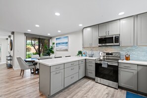 A modern kitchen with grey cabinets, stainless steel appliances, and a large island. - Wailea Ekahi 24B - Modern Garden Retreat w/ Lanai, Split AC & Stylish Renovation (Kihei)