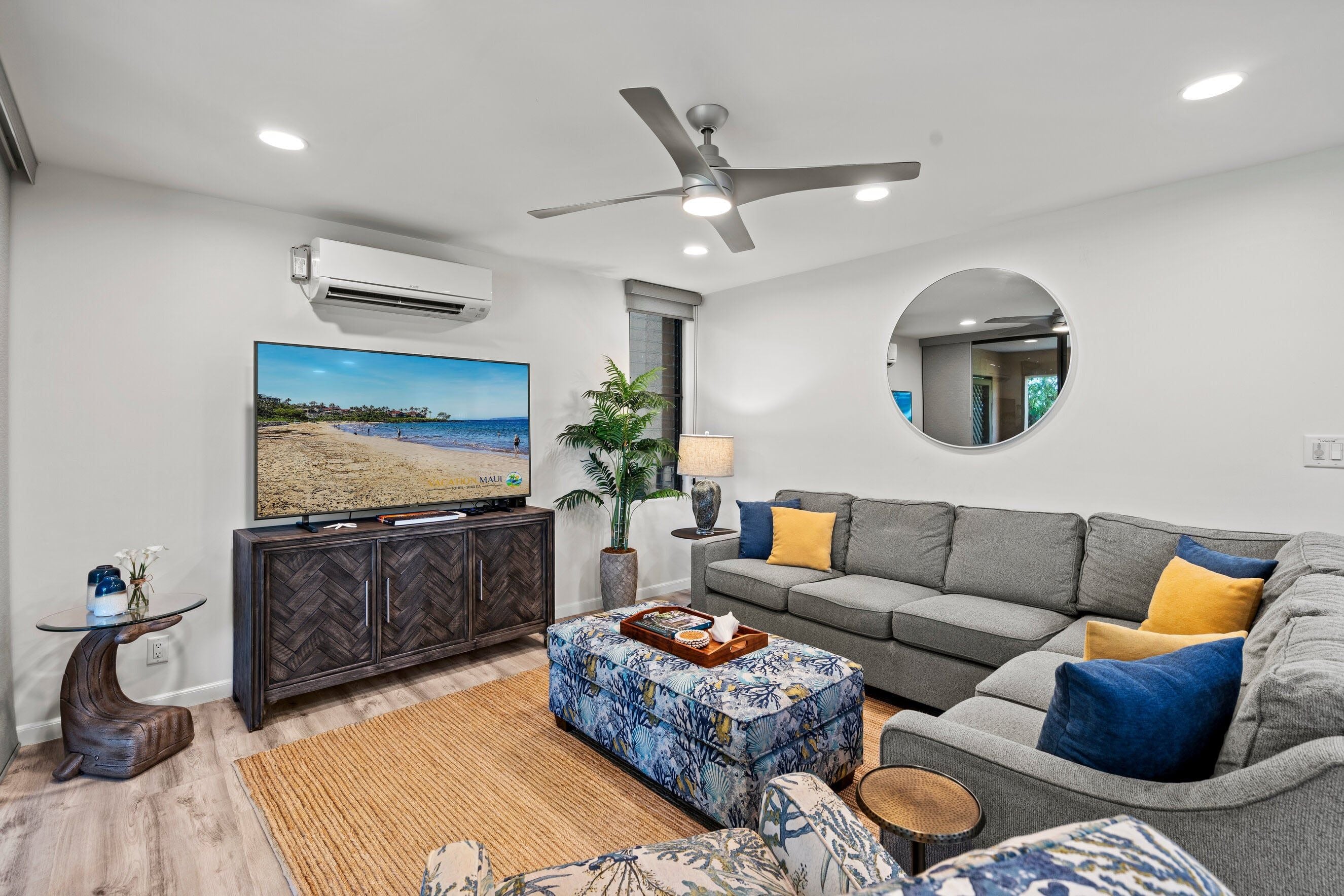 A modern living room with a flat-screen TV, a ceiling fan, and a large window.