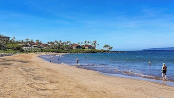 Una playa con cielo despejado, palmeras y un edificio al fondo.