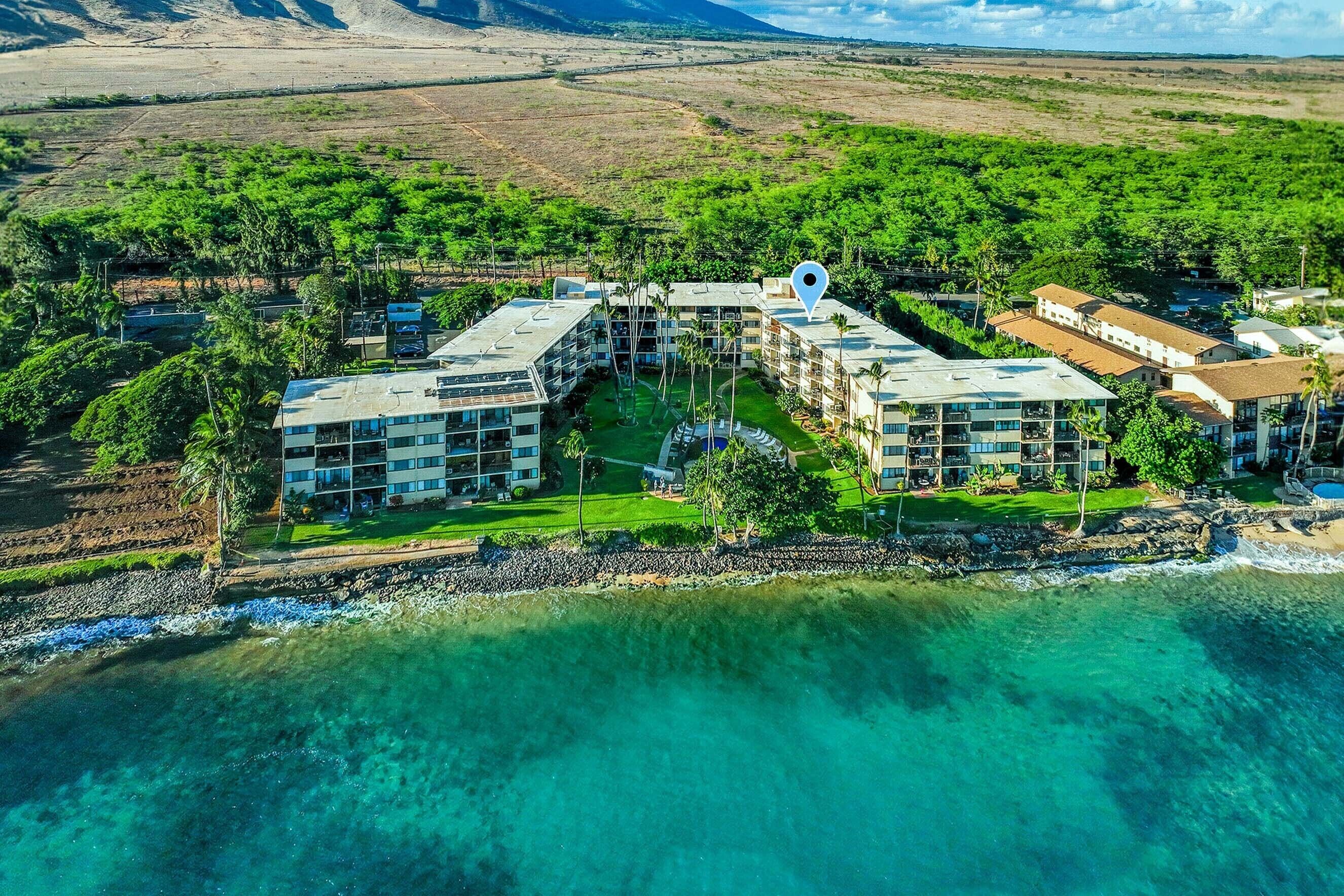 An aerial view of a coastal hotel complex with multiple buildings, a beachfront, and surrounding greenery.
