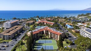 Une station balnéaire comprenant plusieurs bâtiments, un court de tennis et offrant une vue sur l’océan.