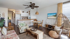 Un salon spacieux comprenant un canapé, une table basse et un coin repas avec des chaises. On peut voir un ventilateur de plafond et un luminaire suspendu.
