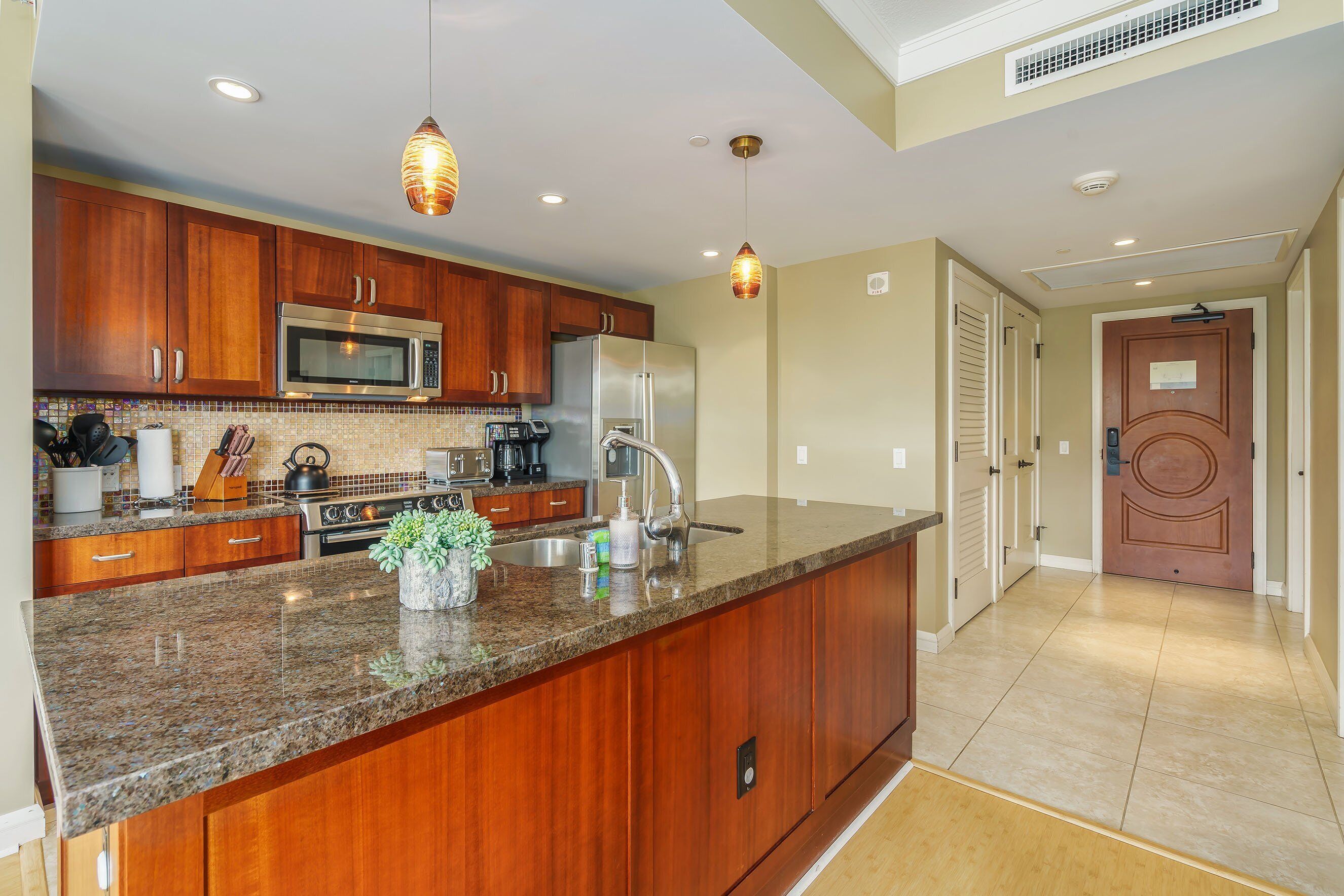 A kitchen with wooden cabinets, a stainless steel refrigerator, and a granite countertop.