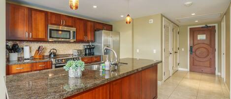 A kitchen with wooden cabinets, a stainless steel refrigerator, and a granite countertop.