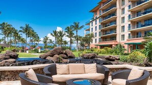 A poolside area with wicker furniture, a view of the ocean, and a building with balconies. - Honua Kai Hokulani 934, Renovated, AC, Large Lanai, No Carpet, Amazing Views! (Lahaina)
