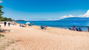 A beach with people sunbathing and swimming, umbrellas, and beach chairs. - Honua Kai Hokulani 934, Renovated, AC, Large Lanai, No Carpet, Amazing Views! (Lahaina)