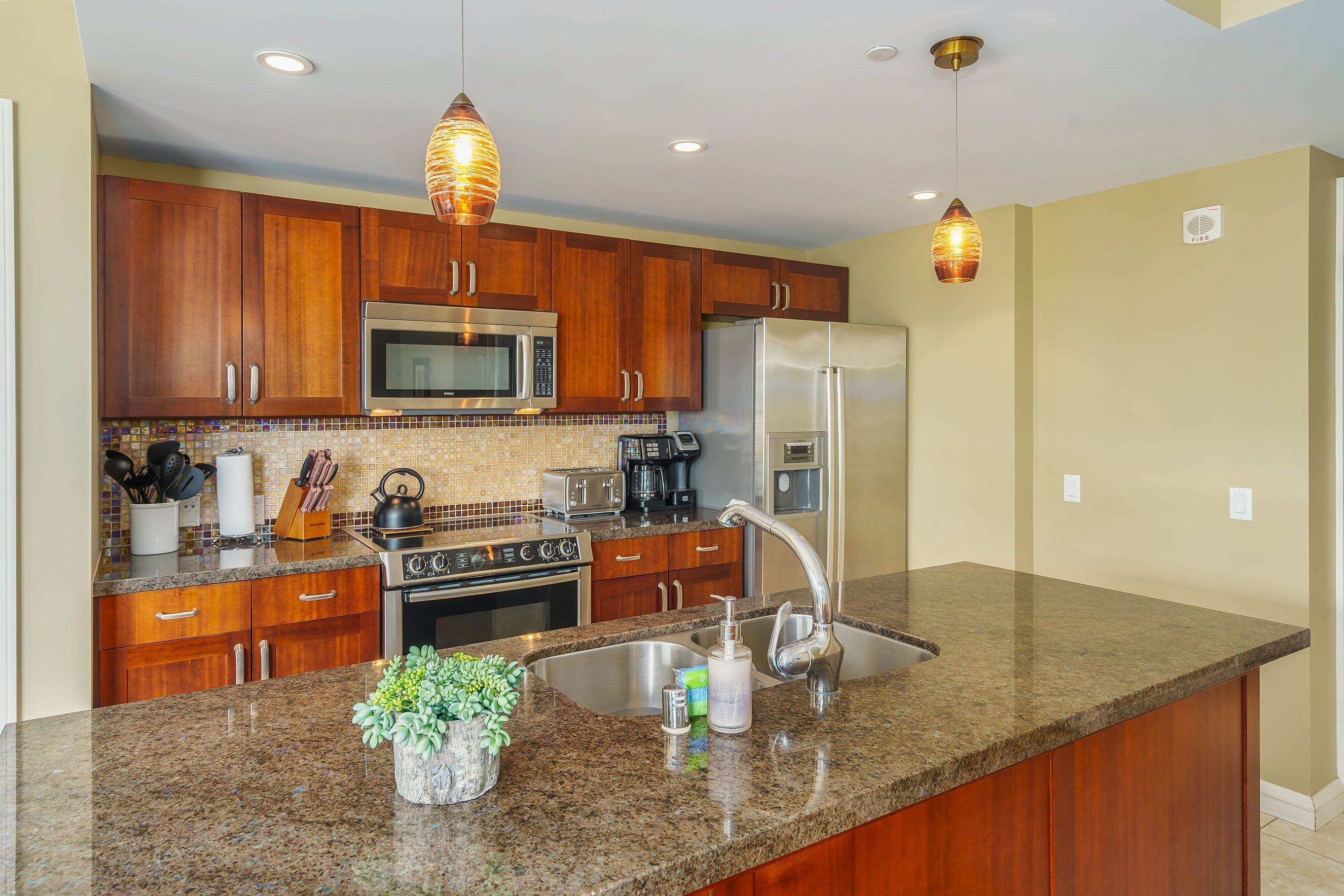 A kitchen with wooden cabinets, stainless steel appliances, granite countertops, and pendant lighting.