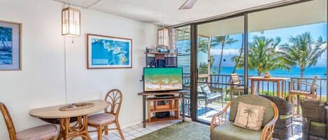 A living room with a TV, wooden furniture, and a view of the ocean.