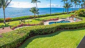 A pool area with a view of the ocean, surrounded by palm trees and well-maintained lawns.
