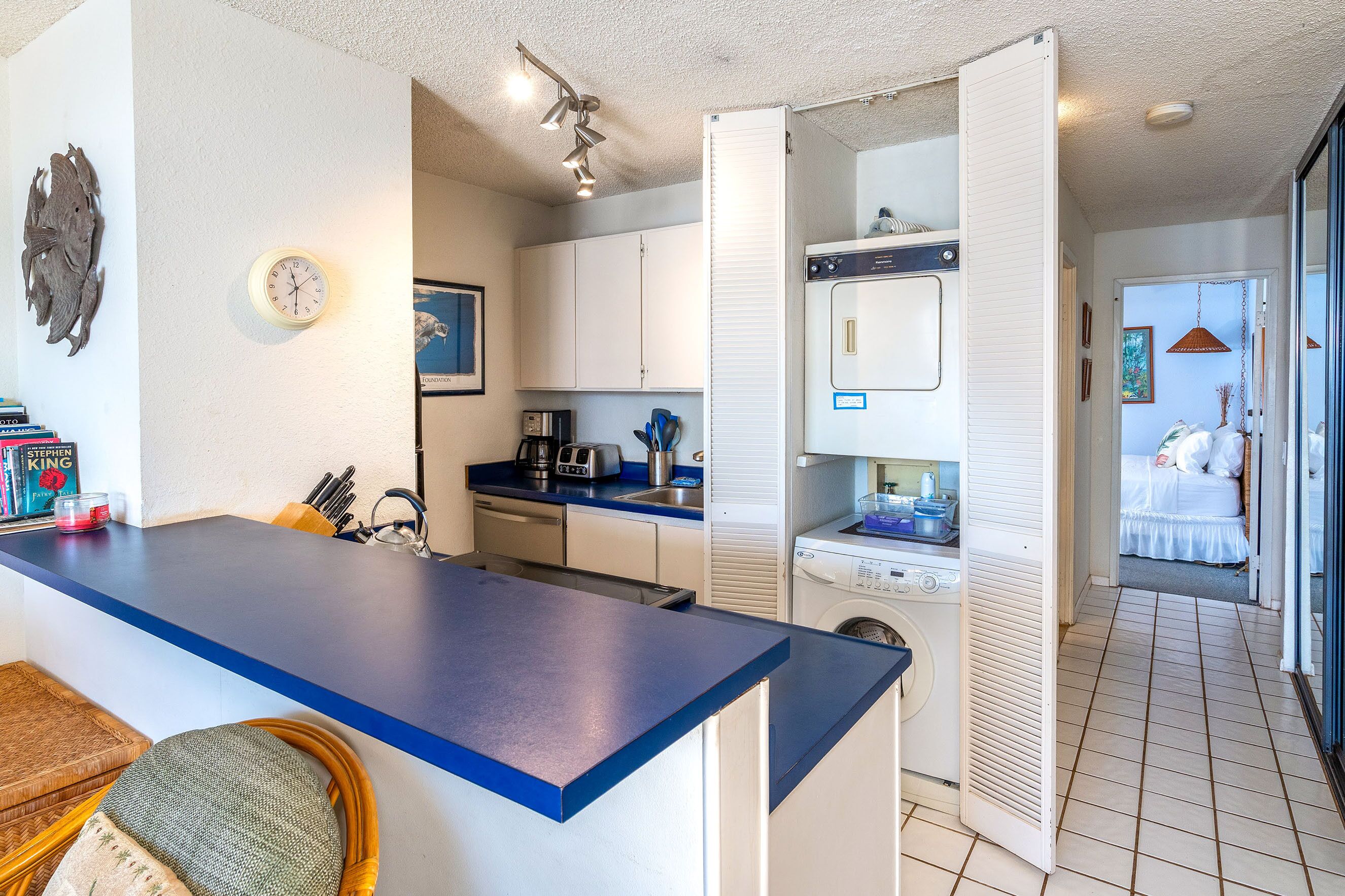 A compact kitchen with a blue countertop, white cabinets, and a washing machine.