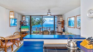 A kitchen with a view of the ocean, a dining area with chairs, a table, and a counter with a kettle.