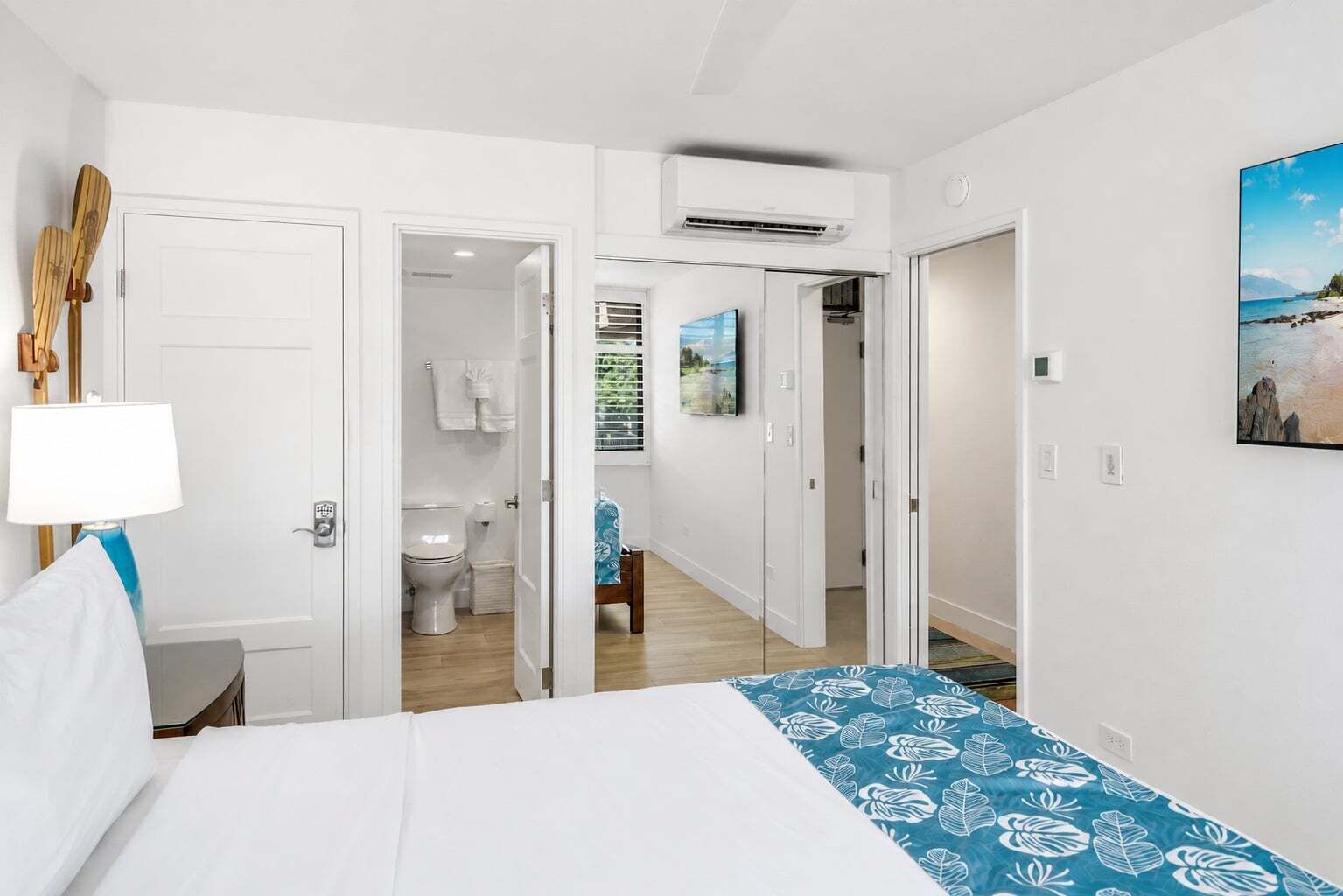 Quarto de hotel com cama, banheiro e corredor que dá para outro quarto.