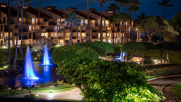 Un hotel de varios pisos con balcones, un jardín ajardinado con fuentes y palmeras.