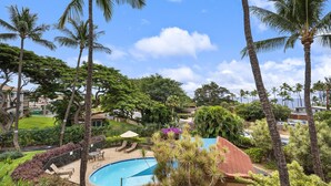 A pool area with palm trees, lounge chairs, and a view of the surrounding landscape. - Maui Vista 1-308 - Steps From the Beach, Renovated, Ocean Views, New Windows, AC (Kihei)