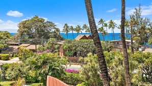 A coastal property with a view of the ocean, surrounded by palm trees and lush greenery. - Maui Vista 1-308 - Steps From the Beach, Renovated, Ocean Views, New Windows, AC (Kihei)