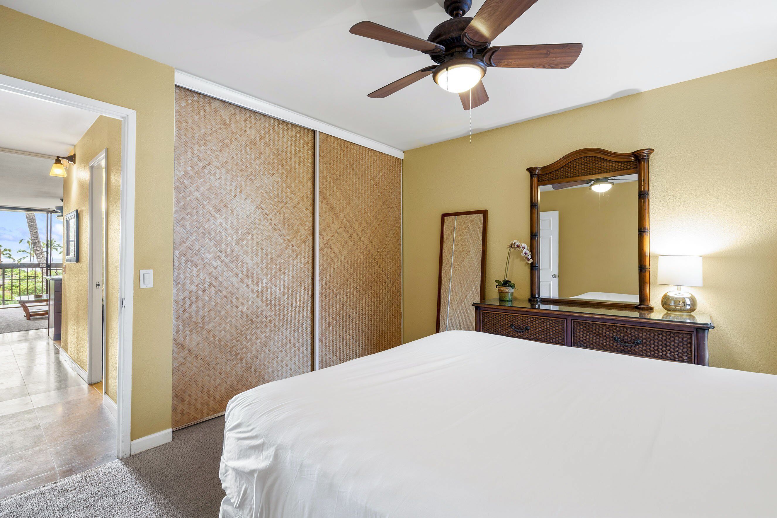 A hotel room with a bed, a ceiling fan, a large mirror, and a view of the outside.