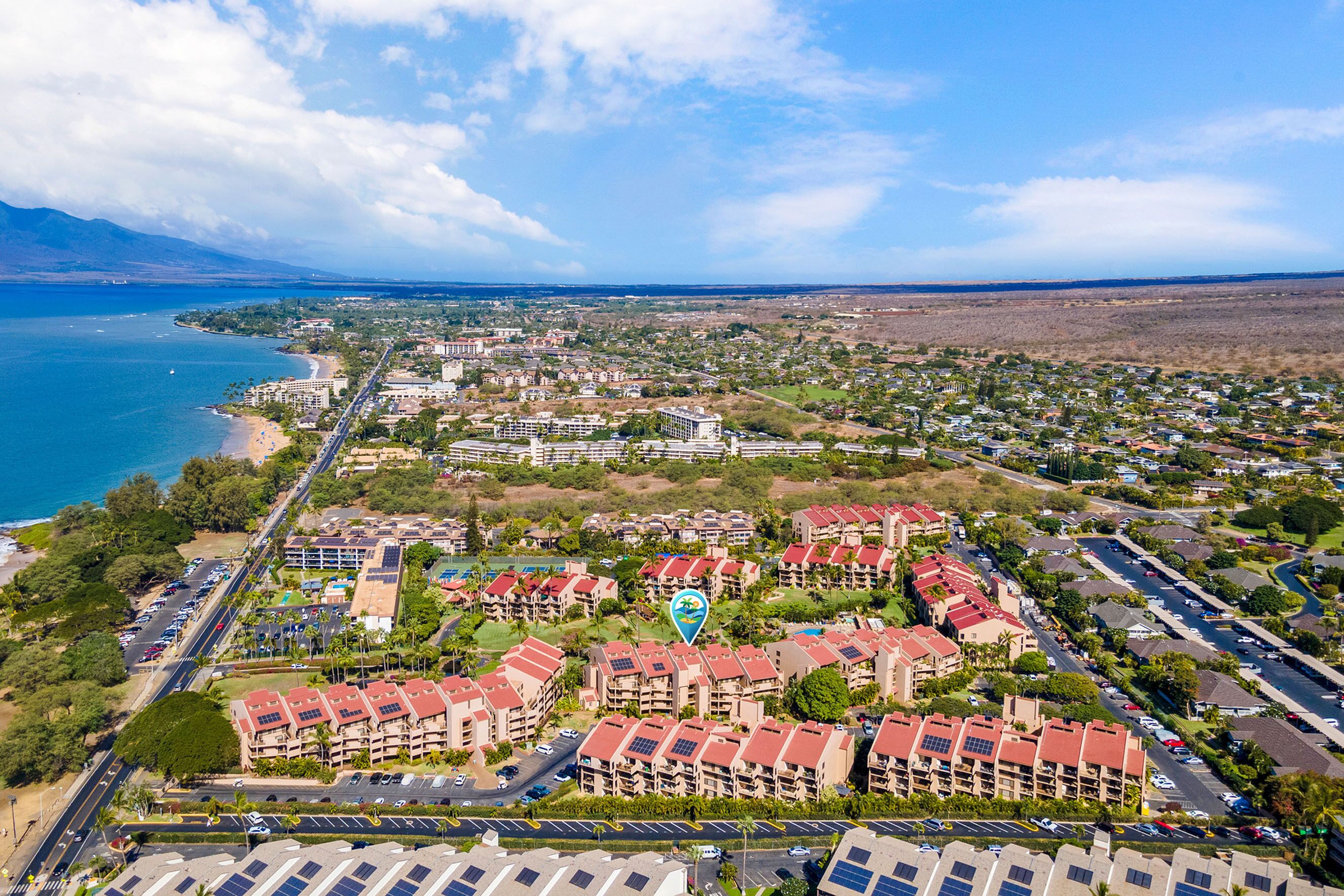 Vista aérea de una zona residencial costera con varios edificios de apartamentos, una playa y cielo despejado.