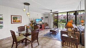 A spacious living area with a dining table, chairs, a sofa, and a TV. - Kamaole Sands 7-206 - Renovated, Courtyard Views, Steps to the Beach, AC (Kihei)