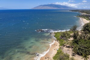 Ein Küstenstrand mit klarem Wasser, einem Sandstrand und einem Berg im Hintergrund.