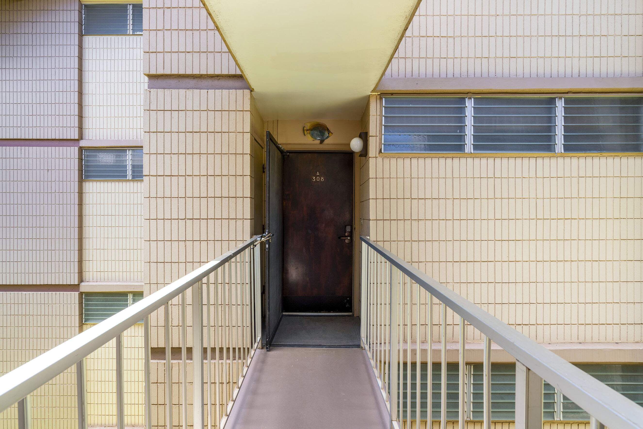 Un escalier étroit et fermé mène à une porte de couleur sombre, sur laquelle on peut voir le numéro 308.