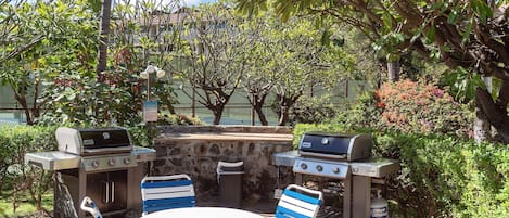 Un patio exterior con dos parrillas Weber, una mesa y sillas azules y blancas.