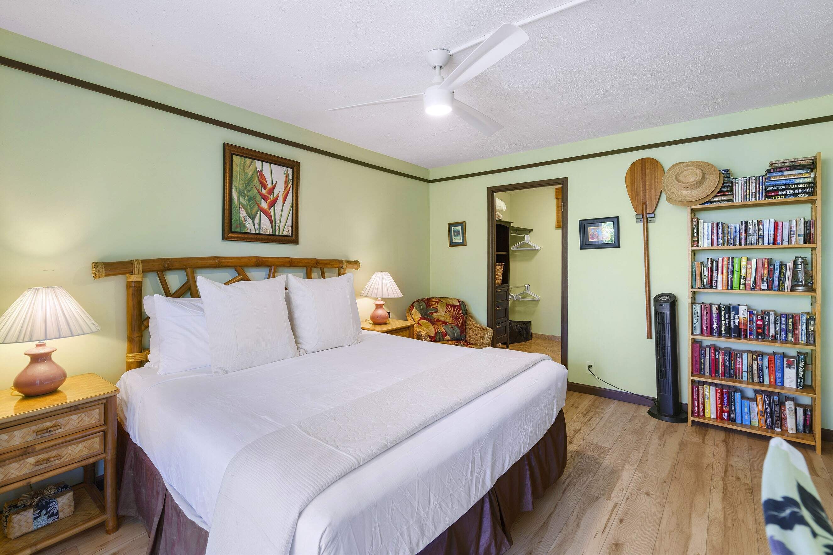 Une chambre à coucher avec un lit, des tables de chevet, une bibliothèque et un ventilateur de plafond.