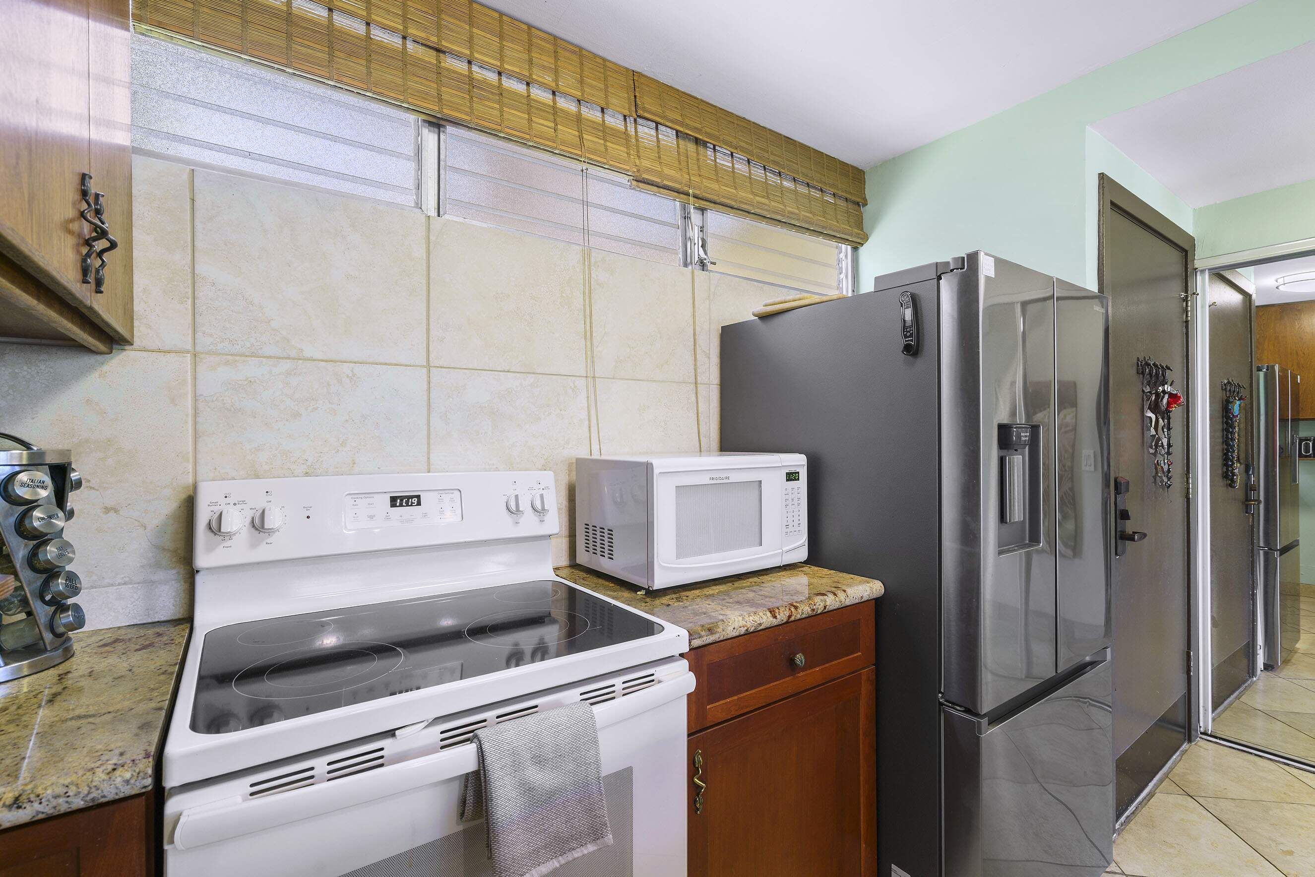 A kitchen with a stove, microwave, refrigerator, and a window with blinds.