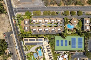 An aerial view of a residential complex with multiple buildings, a swimming pool, tennis courts, and a parking area. - Haleakala Shores A-308 - Ocean/mountain Views, Stylish 2br/2ba, Lanai, AC, Wi-fi (Kihei)