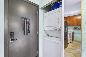 A laundry room with a washing machine, dryer, and a door with a metal hook holding keys. - Haleakala Shores A-308 - Ocean/mountain Views, Stylish 2br/2ba, Lanai, AC, Wi-fi (Kihei)