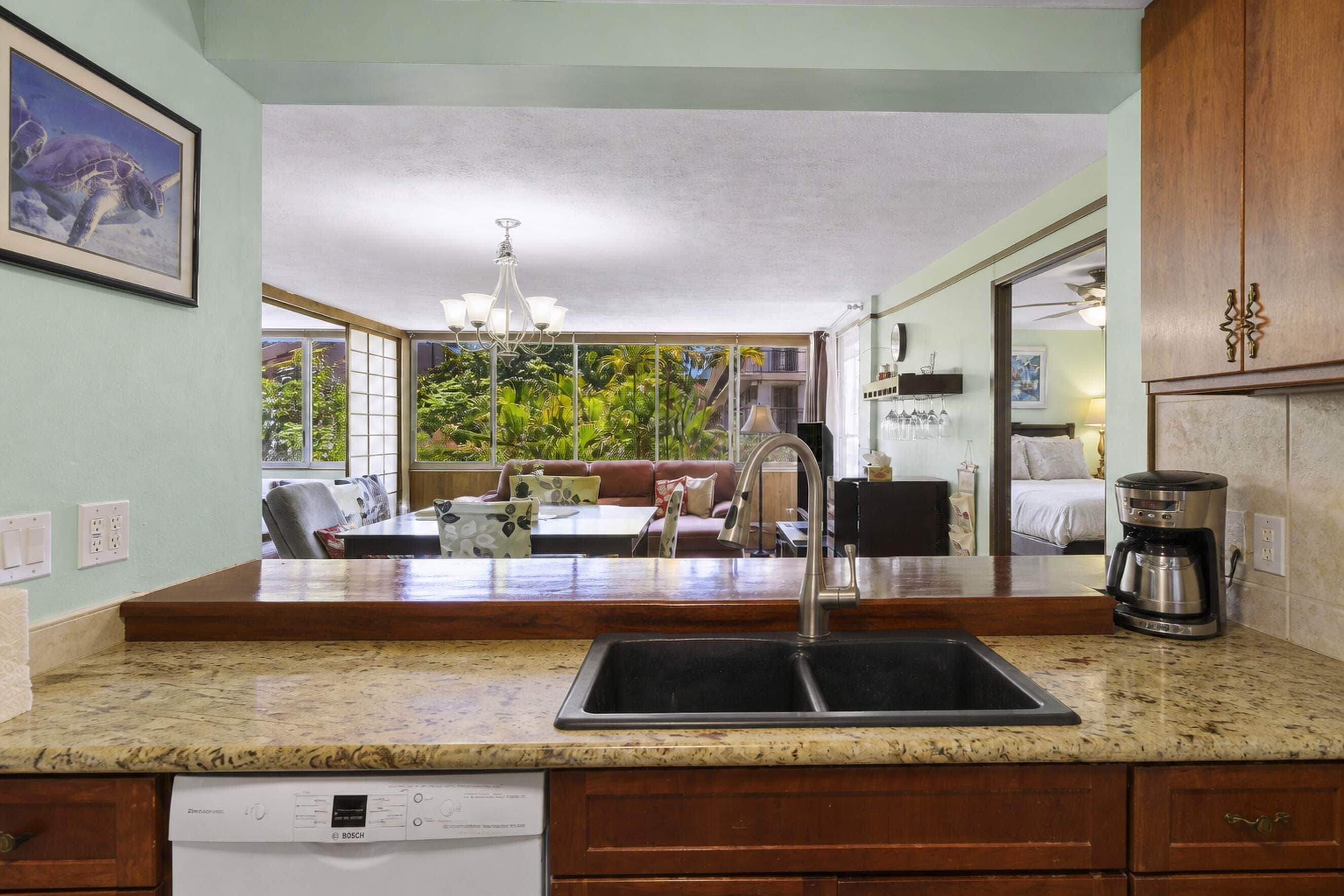 A kitchen with a built-in dishwasher, a coffee maker, and a view of a balcony with a dining area.