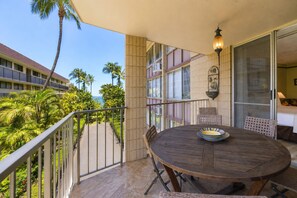Ein Balkon mit Holztisch und -stühlen, mit Blick auf einen tropischen Garten und ein Gebäude mit vielen Fenstern.