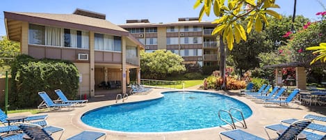 A swimming pool with lounge chairs and a building with multiple balconies.