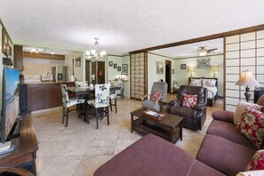 Ein Wohnzimmer mit einer Couch, einem Couchtisch, einem Esstisch mit Stühlen, einer Küchenzeile und einer Schiebetür zu einem anderen Raum.