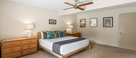 A bedroom with a bed, two bedside tables, a ceiling fan, and wall art.