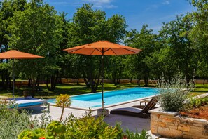 Ein Swimmingpool mit zwei orangefarbenen Sonnenschirmen, umgeben von Bäumen und einer Steinmauer.