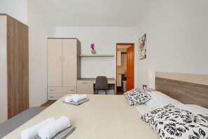 Ein Schlafzimmer mit Bett, Schreibtisch, Stuhl, Kleiderschrank und einem durch eine geöffnete Tür einsehbaren Badezimmer.