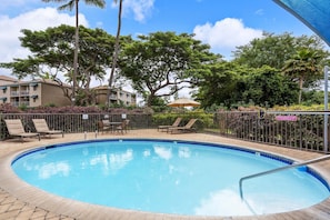 A swimming pool with lounge chairs and a table, surrounded by a fence and trees. - Maui Vista 3-102 - Updated, Ground Level, Steps to the Pool, Walk to Everything! (Kihei)