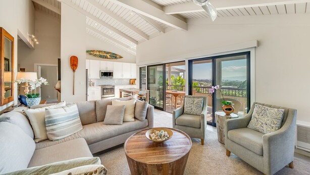 A spacious living area with a large sofa, armchairs, and a coffee table. A kitchen is visible in the background, and there is a balcony with a view. - Extraordinary Molokini Views, Spectacular Renovation, New Split AC, Ocean Views! (Kihei)