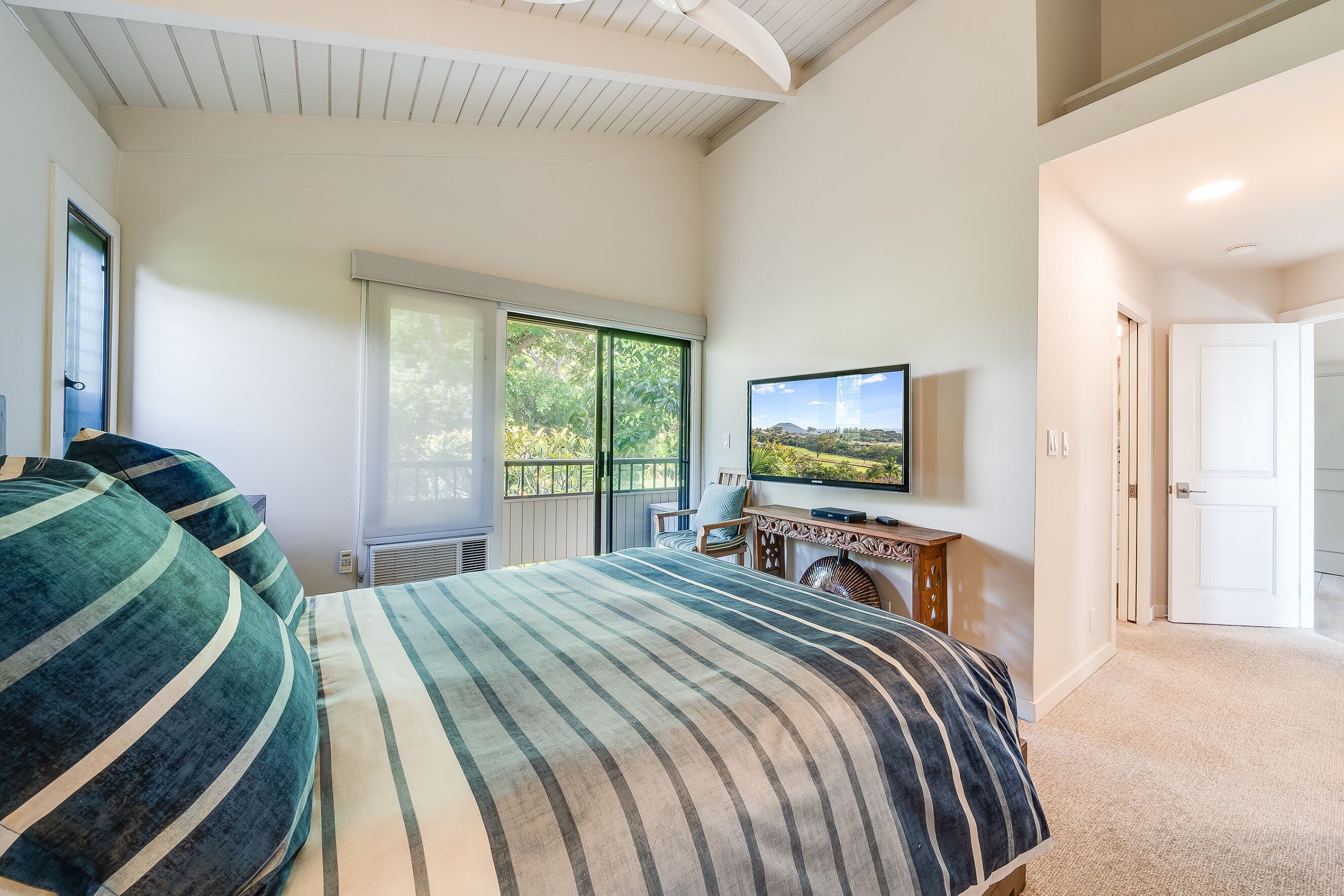 A bedroom with a bed, a television, and a view of the outdoors.
