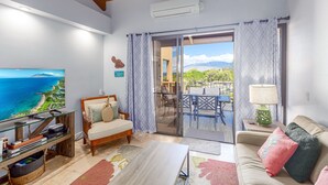 A living room with a television, sofa, and a view of the outdoors. - Kamaole Sands 10-403 - Stunning Renovation - Penthouse Level - Split AC - Look! (Kihei)